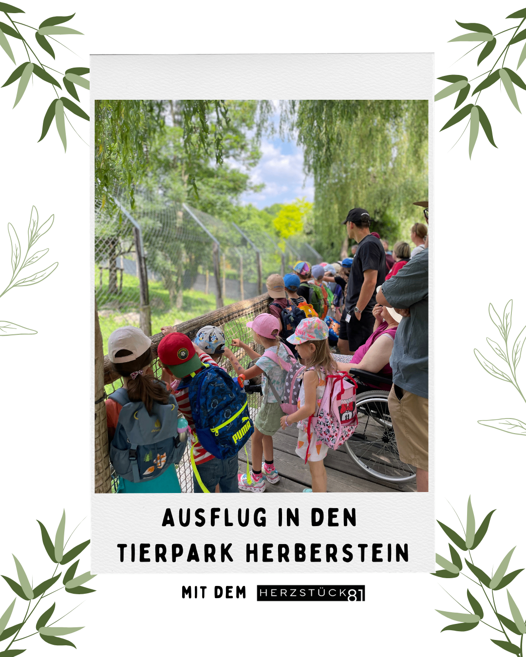 Eine Gruppe von Kindern und Erwachsenen auf einer Holzbrücke in einem Zoo, die Tiere beobachten. Die Kinder tragen Mützen und Rucksäcke. Der Zoo ist von Bäumen und Pflanzen umgeben.