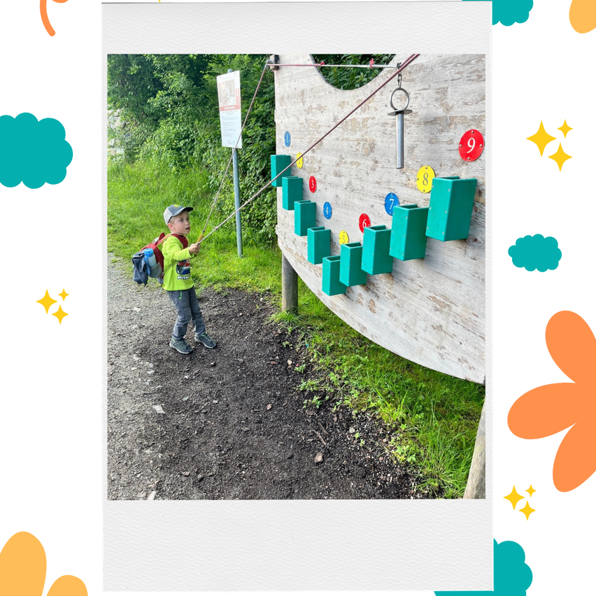 Ein Junge mit Rucksack klettert eine nummerierte Wand mit einer Schnur und einer Seilrolle.