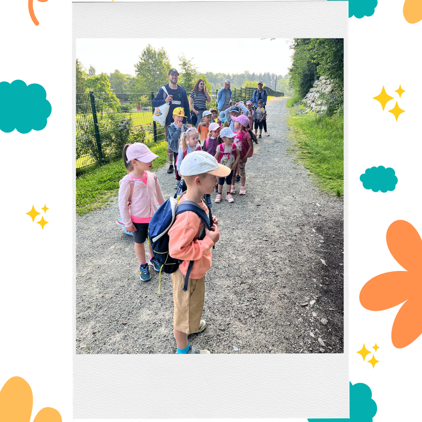 Eine Gruppe von Kindern und Erwachsenen, die auf einem Kiesweg gehen, mit Bäumen und einem Zaun im Hintergrund.