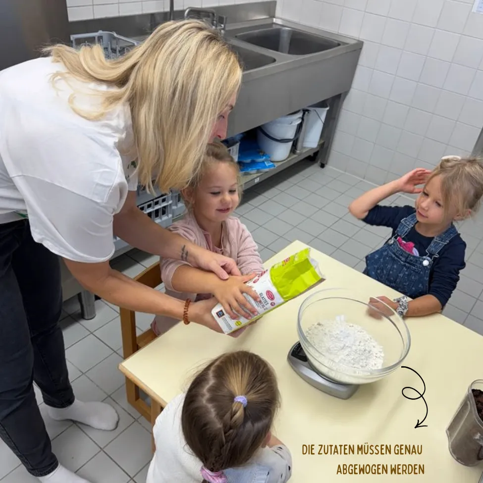 Eine Frau und drei junge Mädchen sind in einer Küche. Die Frau bringt den Mädchen das Backen bei. Das Mädchen auf der linken Seite gießt Mehl in eine Schüssel. Das Mädchen in der Mitte hält eine Tüte Mehl. Das Mädchen auf der rechten Seite schaut zu.