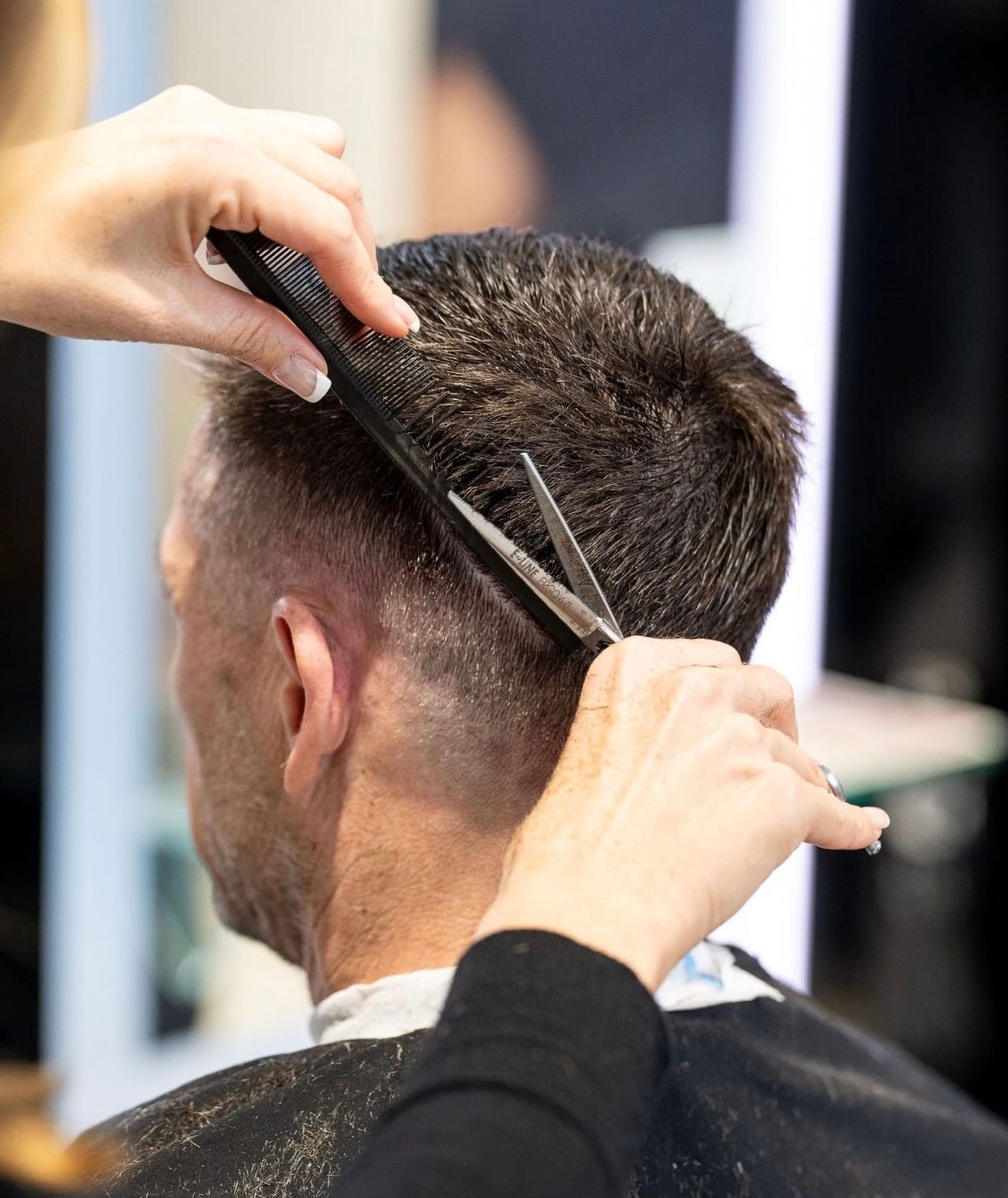 Ein Friseur schneidet die Haare eines Mannes in einem Salon mit Schere und Kamm.