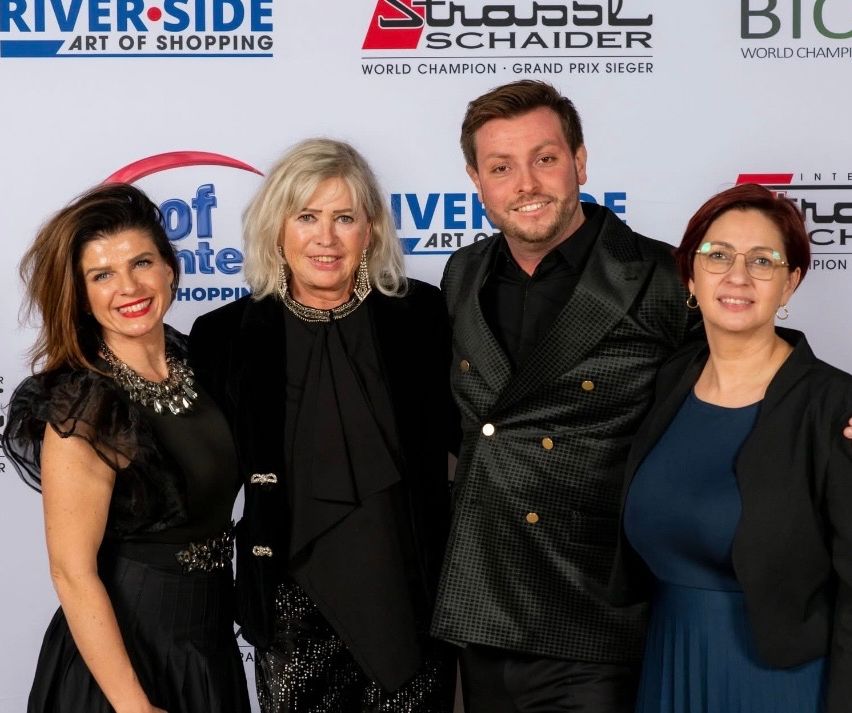 Vier Personen stehen für ein Foto vor einem weißen Banner mit Text und lächeln in die Kamera.