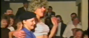 Eine Frau mit lockigem Haar tanzt bei einer Veranstaltung, umgeben von anderen in formeller Kleidung.