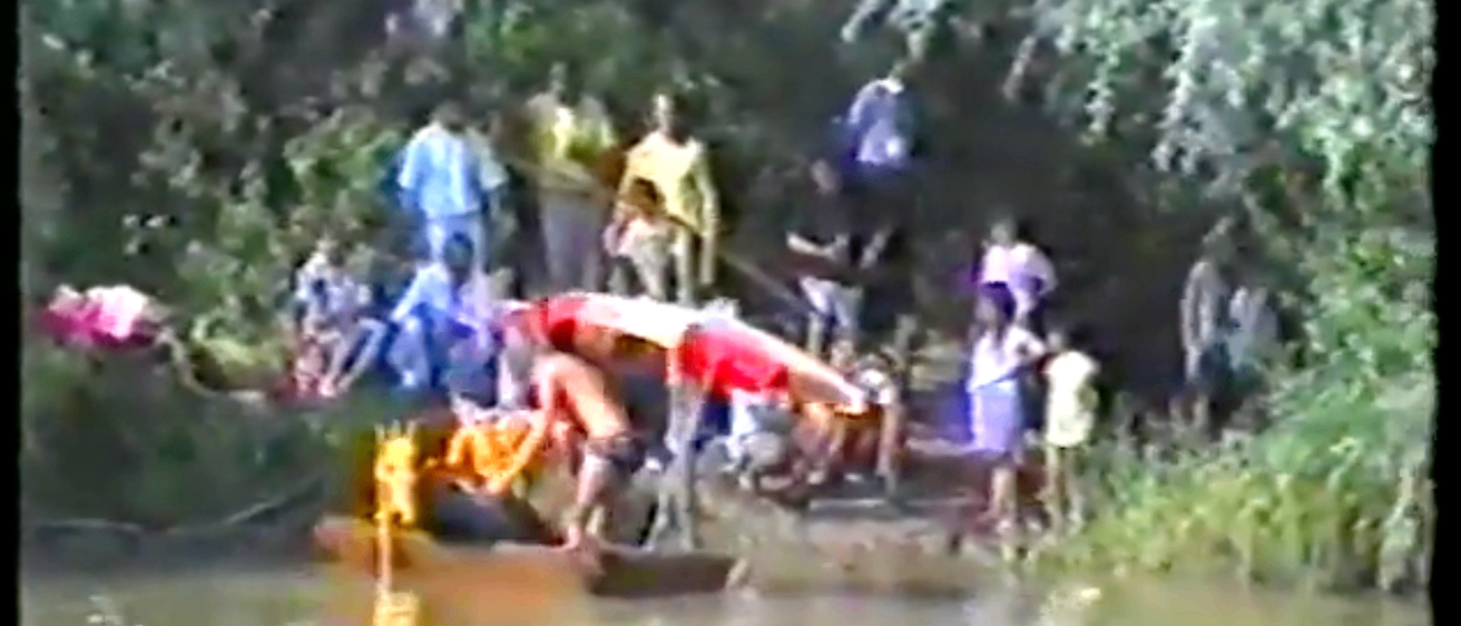 Eine Gruppe von Menschen versammelt sich um ein Kanu in einem Fluss, wobei sich eine Person über das Kanu beugt.