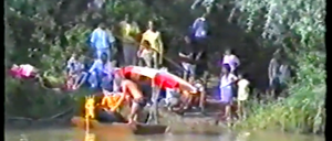 Eine Gruppe von Menschen versammelt sich um ein Kanu in einem Fluss, wobei sich eine Person über das Kanu beugt.