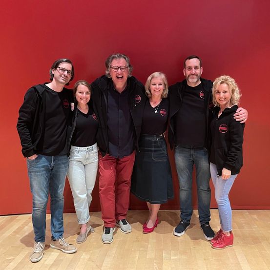 Eine Gruppe von Menschen in schwarzen Kleidungsstücken mit roten Logos posiert für ein Foto vor einer roten Wand.