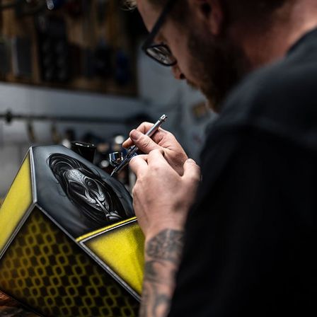 Ein Mann sprüht ein sechseckiges Objekt mit einem Gesicht darauf in einer Werkstatt.