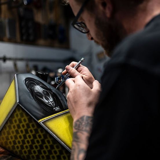 Ein Mann sprüht ein sechseckiges Objekt mit einem Gesicht darauf in einer Werkstatt.