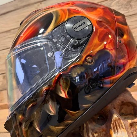 Ein Shark-Helm mit Flammendesign liegt auf einem Schädel. Er hat eine transparente Visier und ein silbernes Logo an der Seite.