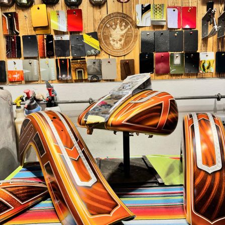 Ein Werkstattraum voller verschiedener farbiger Farbmuster und Motorradteile, der ein orangefarbenes und weißes lackiertes Motorradteil zur Schau stellt.