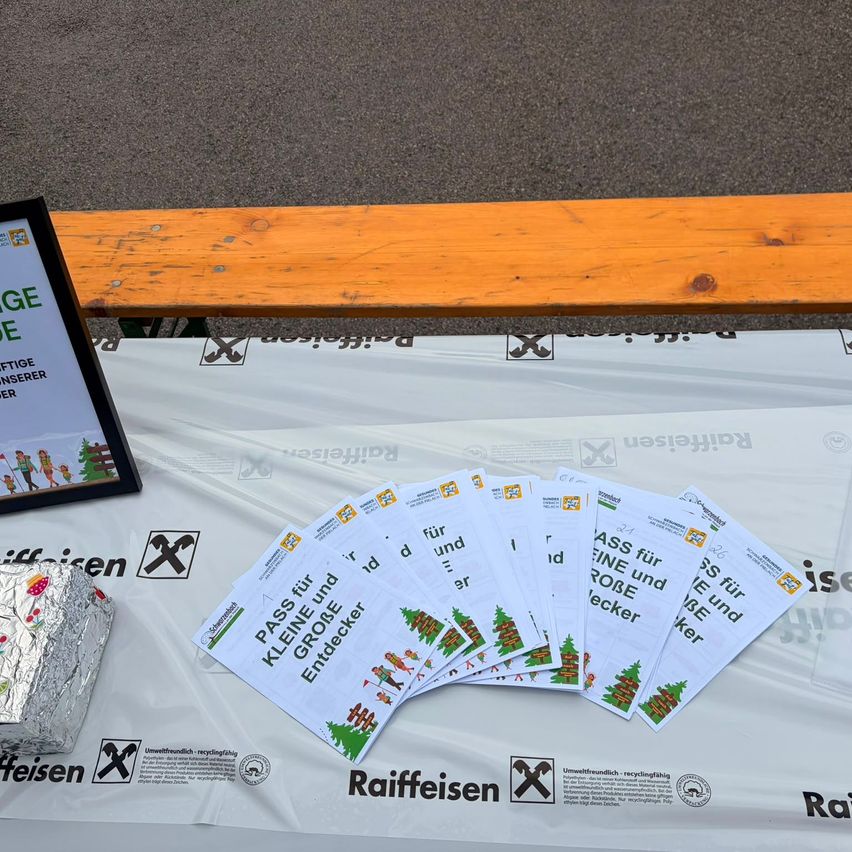Ein Tisch mit einer weißen Abdeckung zeigt mehrere Flugblätter oben. Ein Holzbank ist im Hintergrund. Die Flugblätter sind mit 'PASS FUER' und 'KLEINEN GROSSEN ENDE' beschriftet.