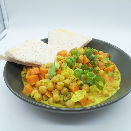 Eine Schüssel mit Kichererbsen-Curry mit Karotten und Frühlingszwiebeln, begleitet von zwei Stücken Fladenbrot.