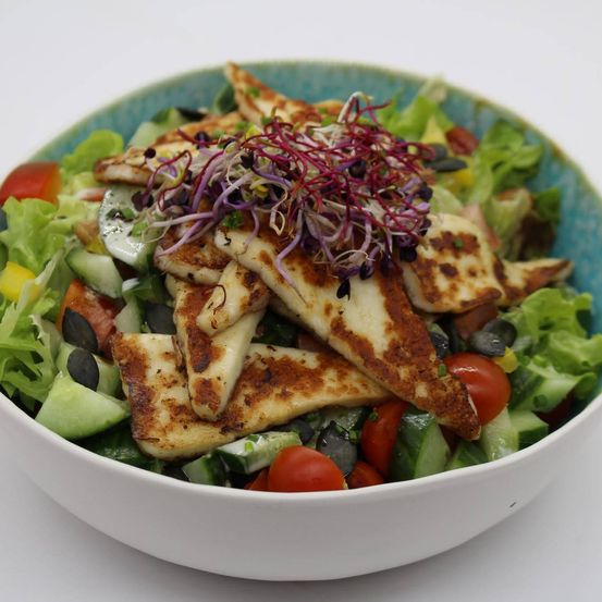 Eine weiße Schüssel gefüllt mit einem frischen Salat, der aus Salat, Tomaten, Gurken und gegrillten Hähnchenstücken besteht, die mit roten Sprossen gekrönt sind.