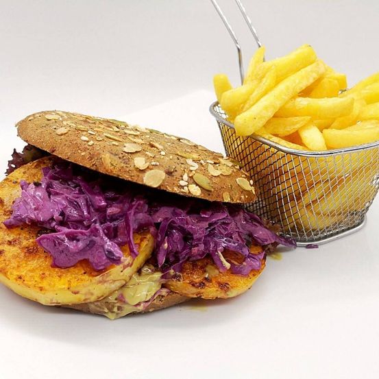 Ein Sandwich mit gebratenen Kartoffelscheiben, rotkohl und einer Beilage Pommes Frites in einem Metallkorb auf weißem Hintergrund.