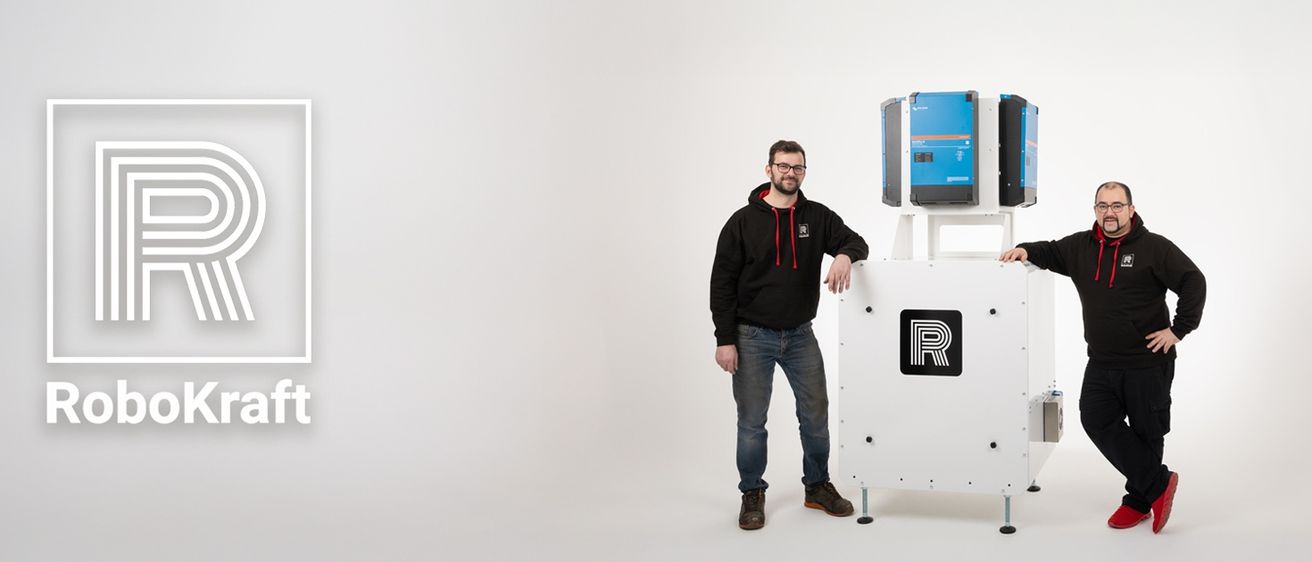 Ein Mann in einer schwarzen Kapuzenjacke und Jeans steht neben einer weißen Maschine mit einem blauen Kasten oben und einem Buchstaben R auf der Seite.