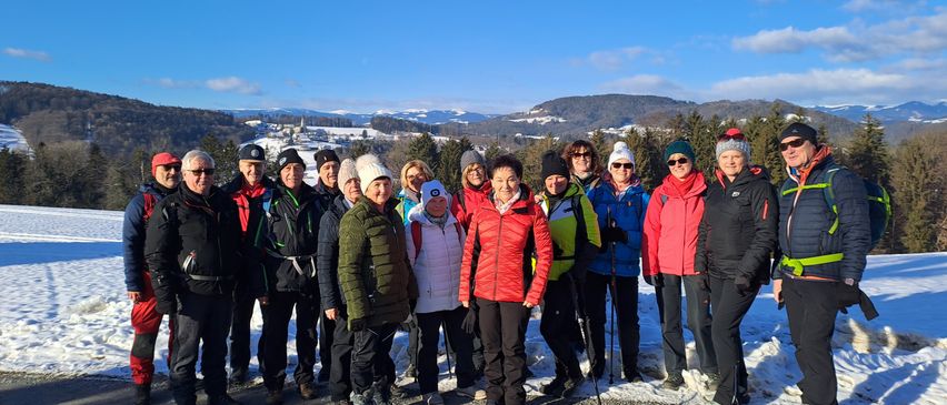 Eine Gruppe von Menschen in Winterkleidung posiert für ein Foto auf einem Schotterweg, mit verschneiten Bergen im Hintergrund.