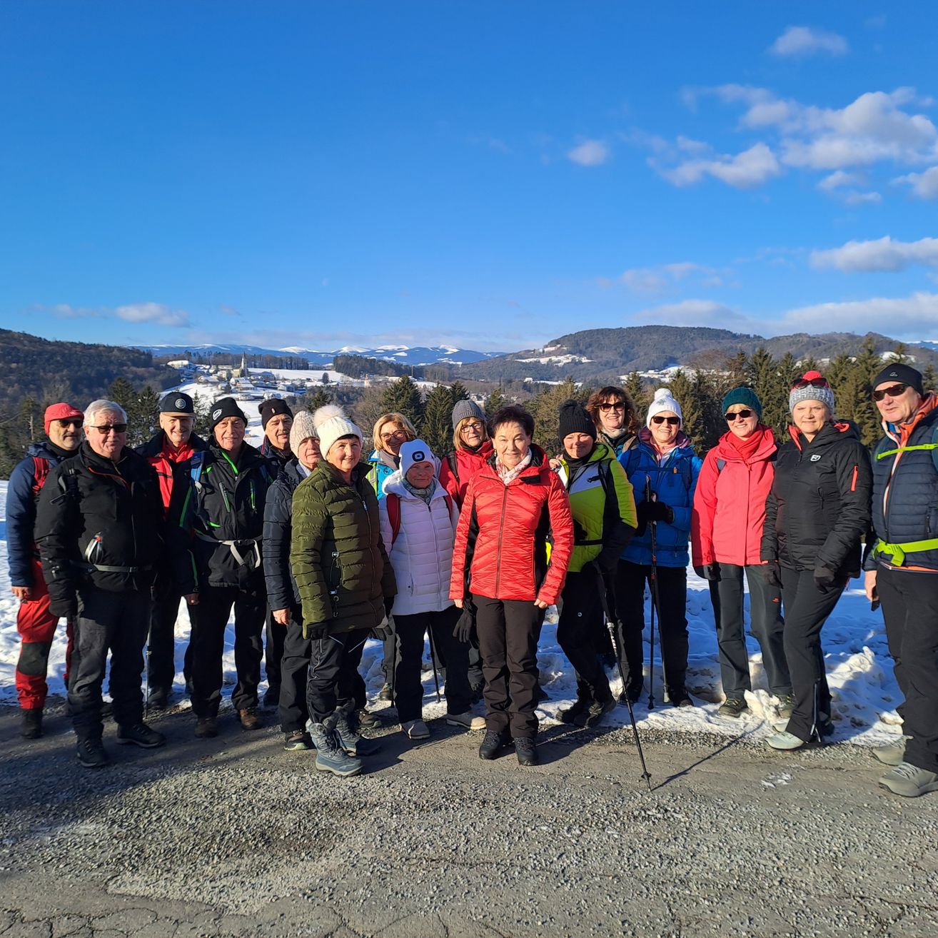 Eine Gruppe von Menschen in Winterkleidung posiert für ein Foto auf einer verschneiten Straße, mit Bergen im Hintergrund.