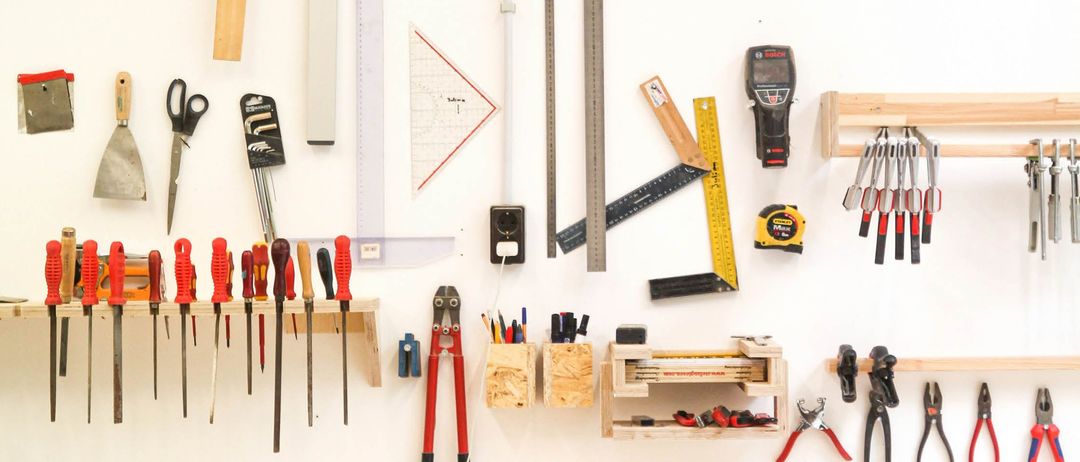 Eine weiße Wand mit verschiedenen Werkzeugen und Geräten befestigt. Beinhaltet Hämmer, Sägen und Messinstrumente.
