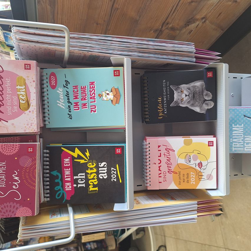 A white shelf with multiple colorful notebooks, including one with a cat on the cover and another with the title 'Ich atme ein'. The notebooks are arranged in a row.