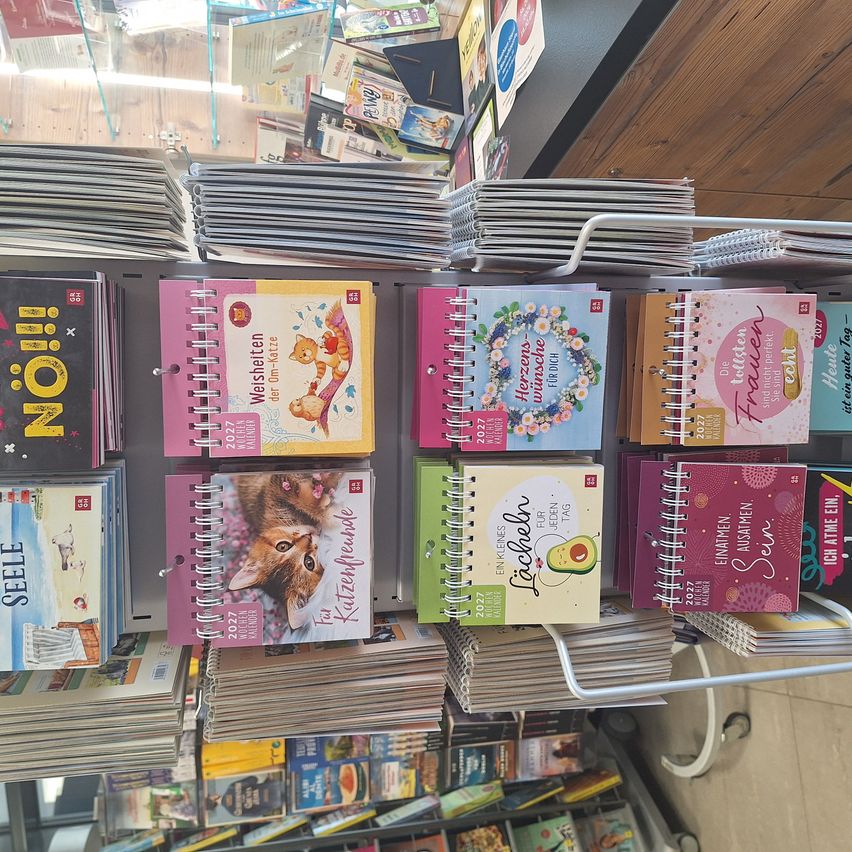 A display of various colorful spiral-bound calendars for the year 2022, including themes like cats, flowers, and avocados, arranged on a shelf in a store.