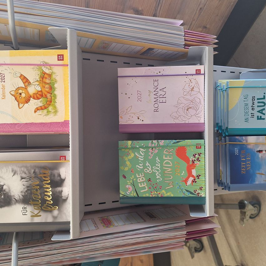 A shelf with various colorful calendars on display. The top left has a cat calendar, the top right has a romance era calendar, and the bottom has a life and wonder calendar.