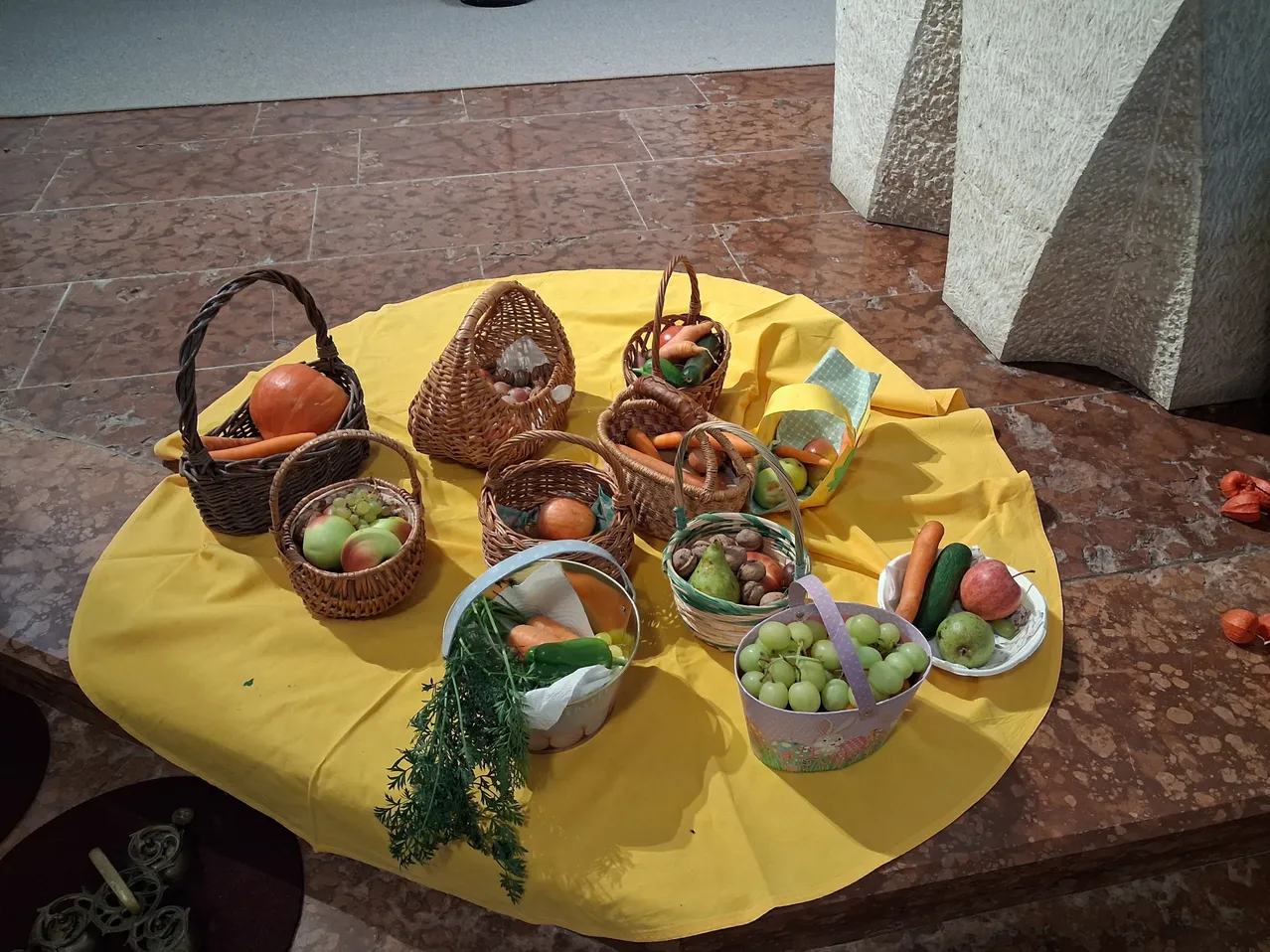 Ein gelber Stoff mit mehreren Weidenkörben, die mit verschiedenen Obst- und Gemüsesorten gefüllt sind.