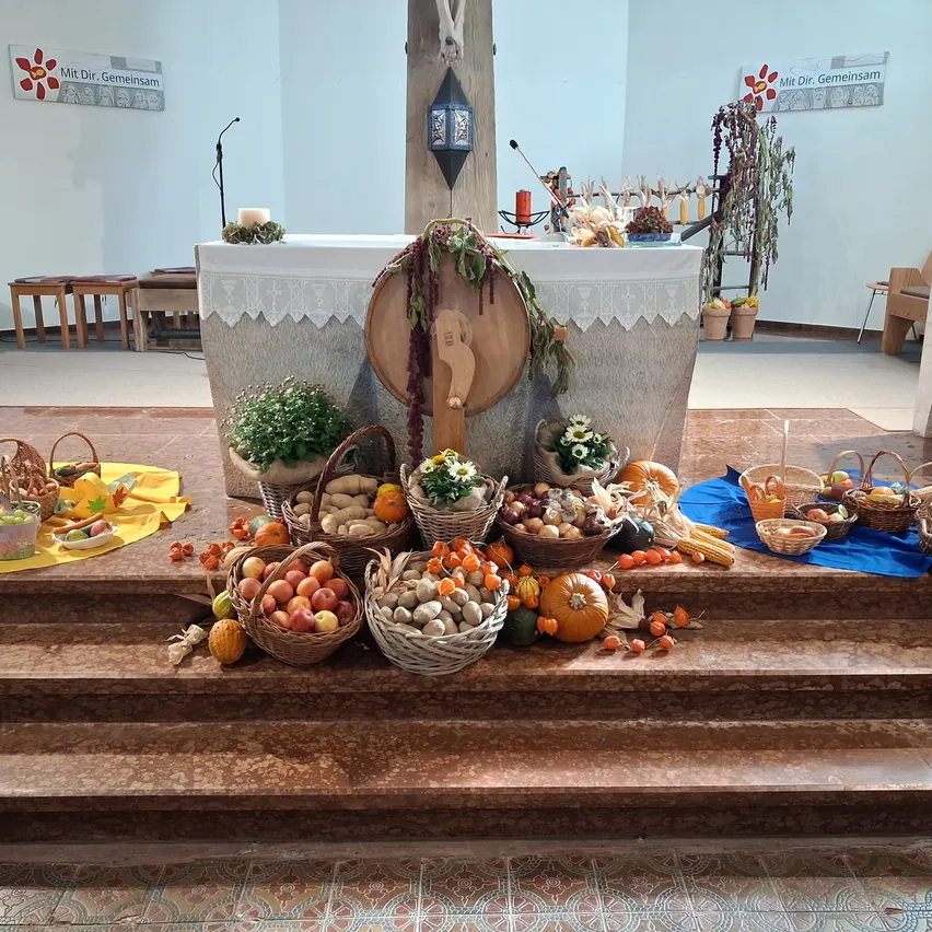 Ein Altar in einer Kirche ist mit einer Vielzahl von Obst und Gemüse geschmückt, darunter Äpfel, Kürbisse und Mais, die in Körben und Schalen angeordnet sind.