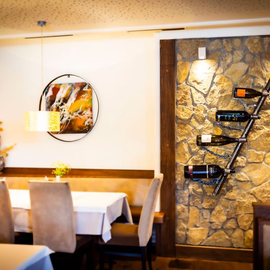 Ein Essbereich mit einem für eine Mahlzeit gedeckten Tisch, einem modernen abstrakten Gemälde an der Wand und einer Steinwand mit einem Weinregal.