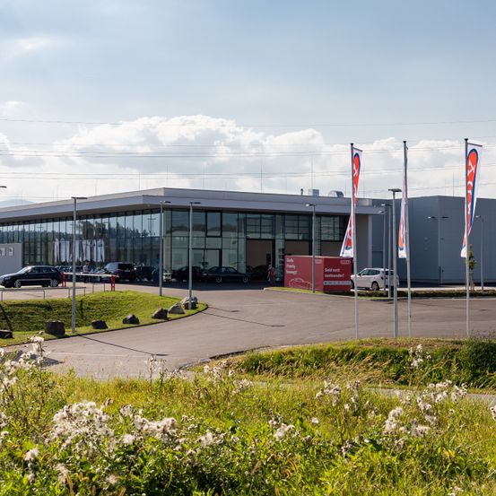 Bild enthält, Architecture, Building, Office Building, Car, Car Dealership, Transportation, Vehicle, Person, Machine, Wheel