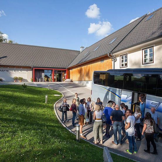 Touristen versammeln sich vor einem modernen Gebäude mit einem geparkten Bus, möglicherweise für eine Tour.