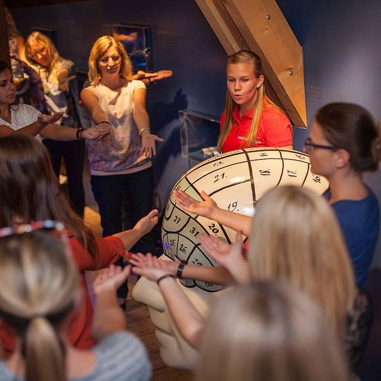 Eine Gruppe von Frauen ist um ein großes Gehirnmodell mit Nummern versammelt und spielt ein Spiel in einer geschlossenen Umgebung.