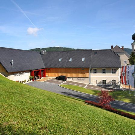 Ein modernes Gebäude mit schwarzem Dach und roten Türen befindet sich auf einem Hügel mit saftigem grünem Gras und einer kleinen Auffahrt.