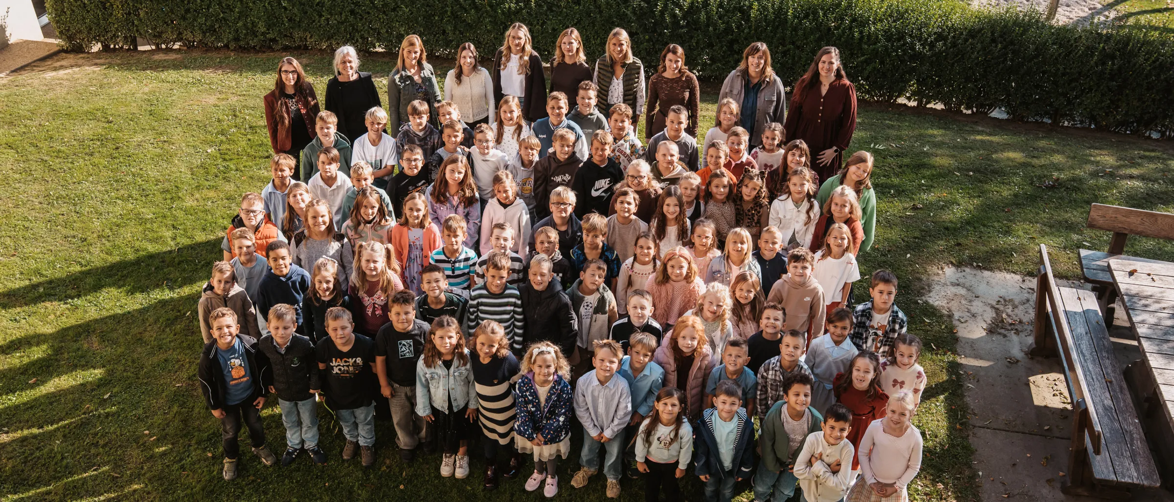 Eine große Gruppe von Kindern und Erwachsenen steht im Kreis auf einem Rasenfeld.