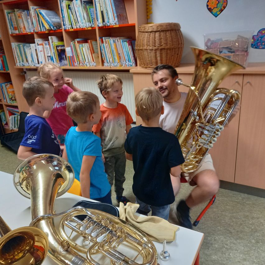 Ein Mann spielt Tuba in einer Bibliothek, während mehrere Kinder zuschauen.