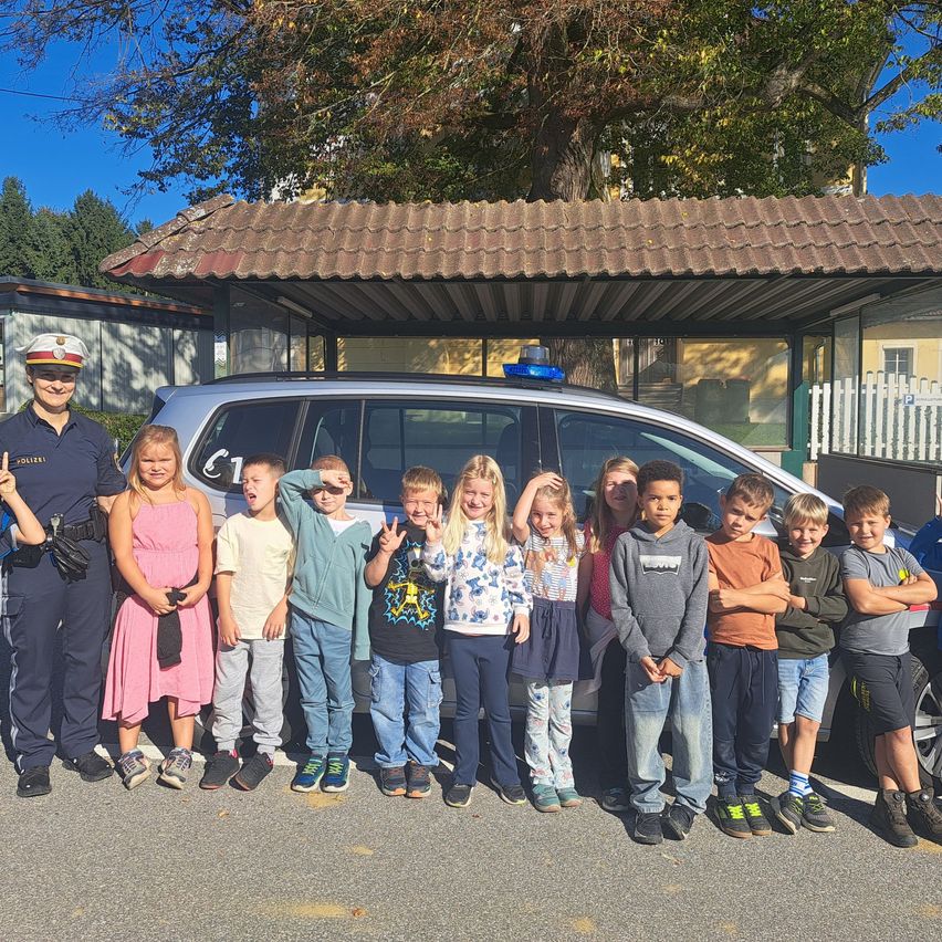 Eine Gruppe von Kindern und einem Polizeibeamten, die vor einem Polizeiauto für ein Foto posieren.