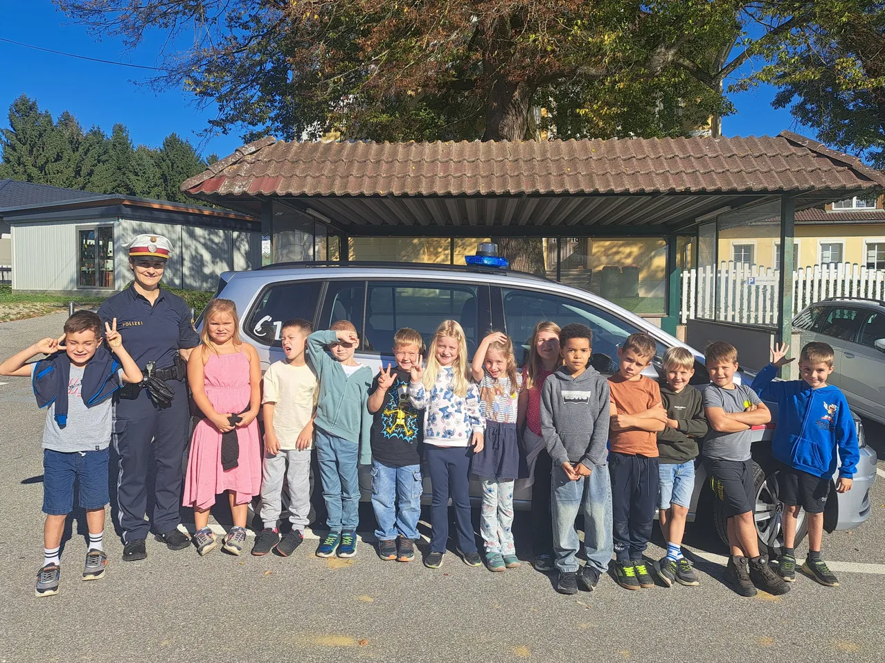 Eine Gruppe von Kindern und einem Polizeibeamten, die vor einem Polizeiauto für ein Foto posieren.