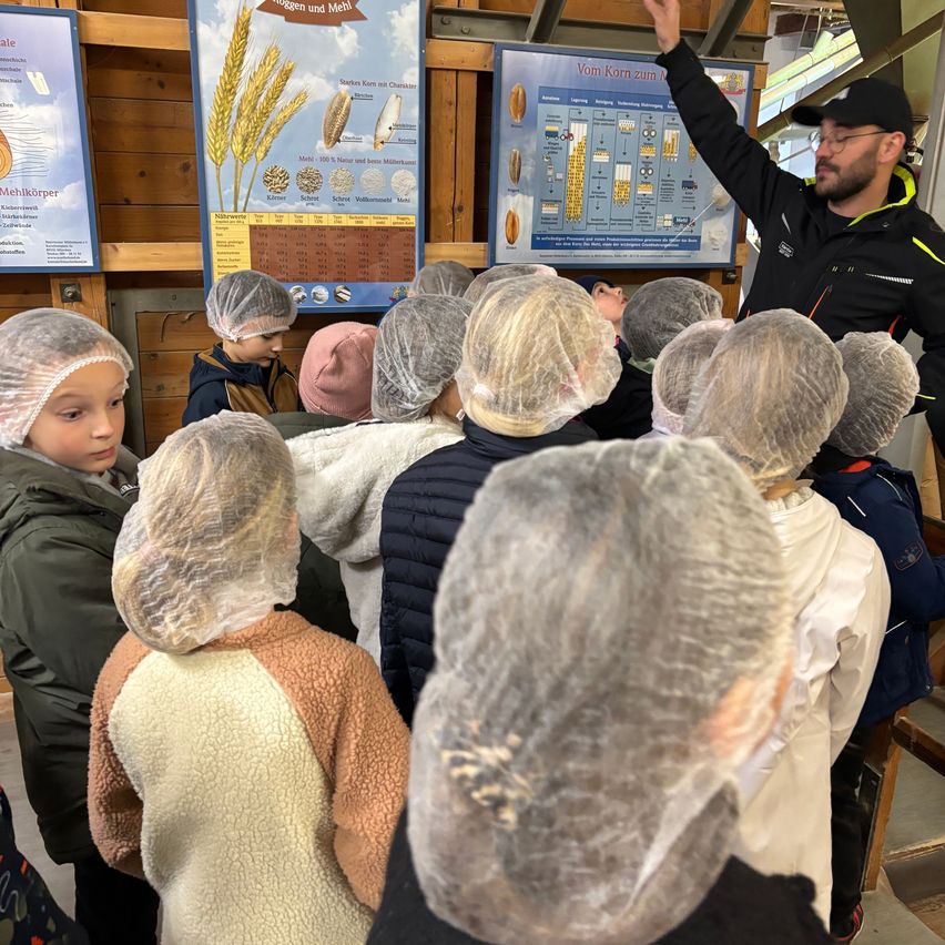 Ein Mann unterrichtet Kinder über Weizen in einem Gebäude, sie tragen alle Haarnetze.