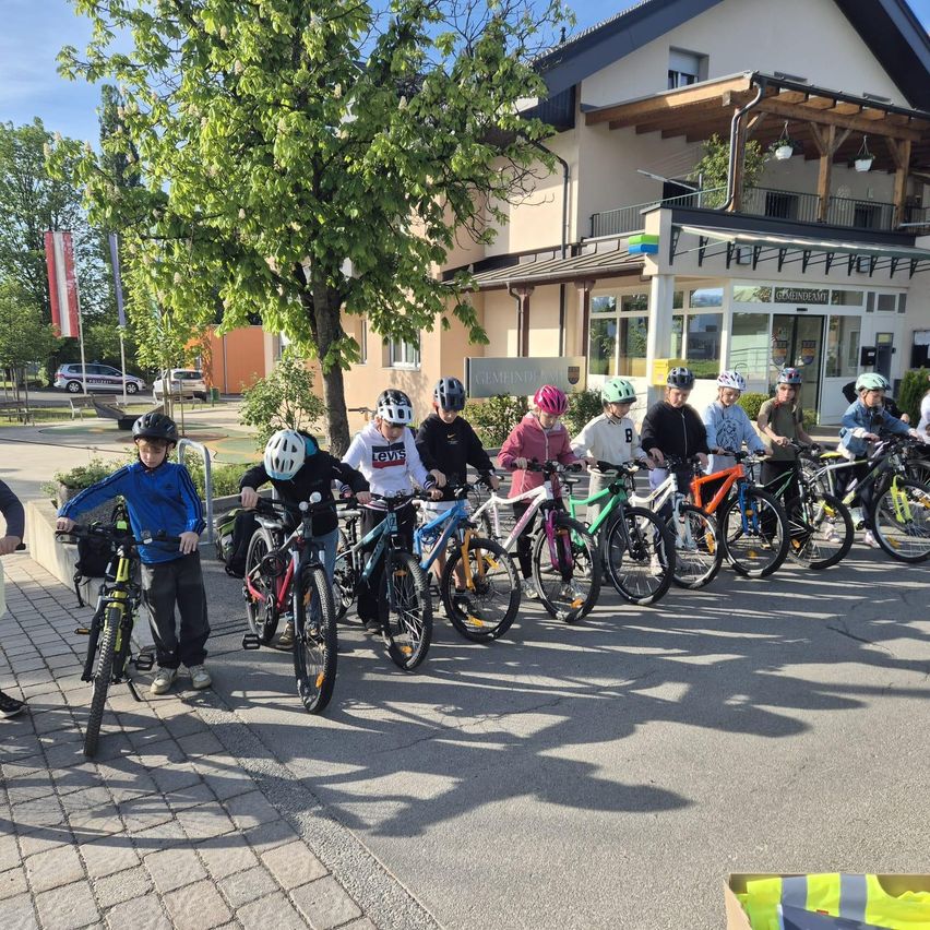 Eine Gruppe von Kindern mit Helmen steht mit ihren Fahrrädern vor einem Gebäude.