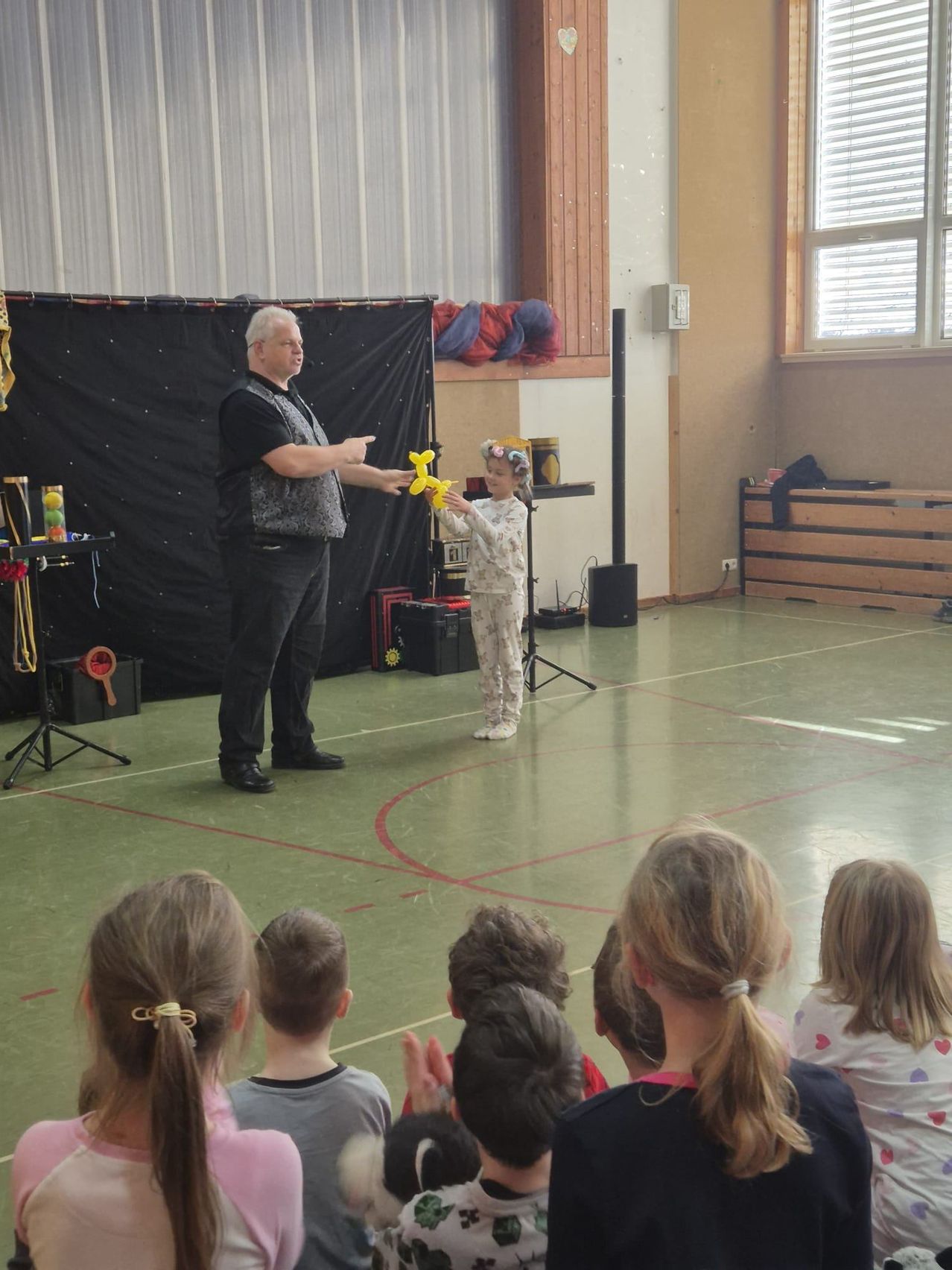 Ein Mann führt einen Ballontrick vor einem kleinen Mädchen und einem Publikum aus Kindern vor.