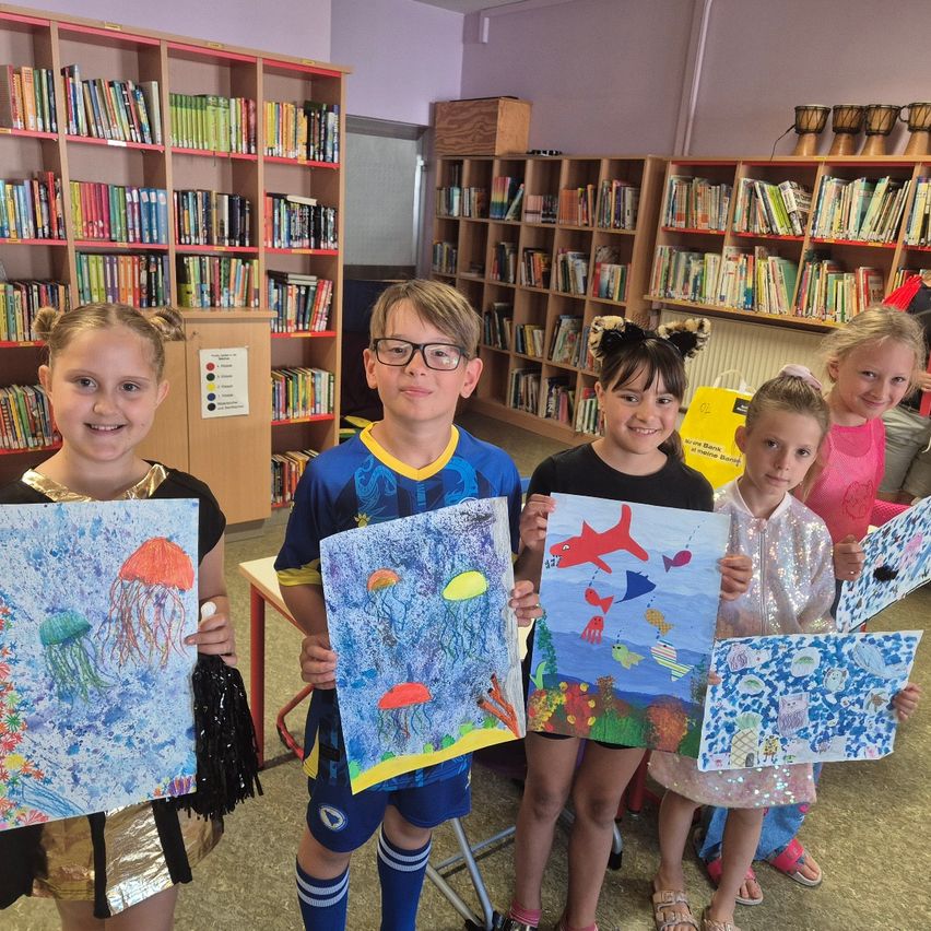 Fünf Kinder in einer Bibliothek, jedes hält ein farbenfrohes Gemälde von Meereslebewesen und posiert für ein Foto.