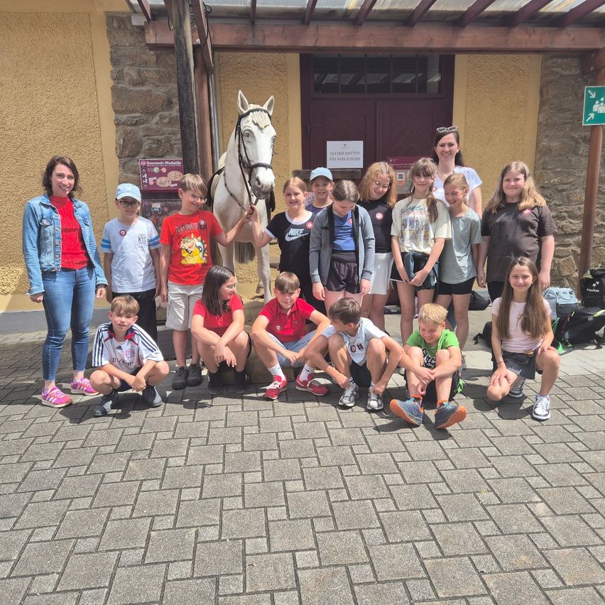 Eine Gruppe von Kindern und Erwachsenen posiert für ein Foto vor einem Gebäude mit einem weißen Pferd.