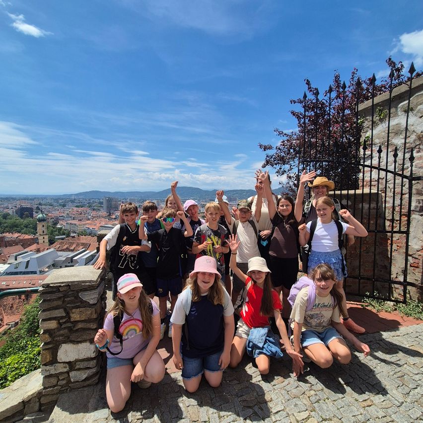 Eine Gruppe von Kindern und zwei Erwachsenen posiert für ein Foto auf einer Steinmauer mit Blick auf eine Stadt.