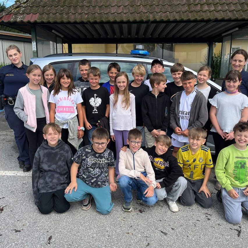 Eine Gruppe von Kindern und zwei Polizeibeamtinnen posiert für ein Foto vor einem Polizeiauto.