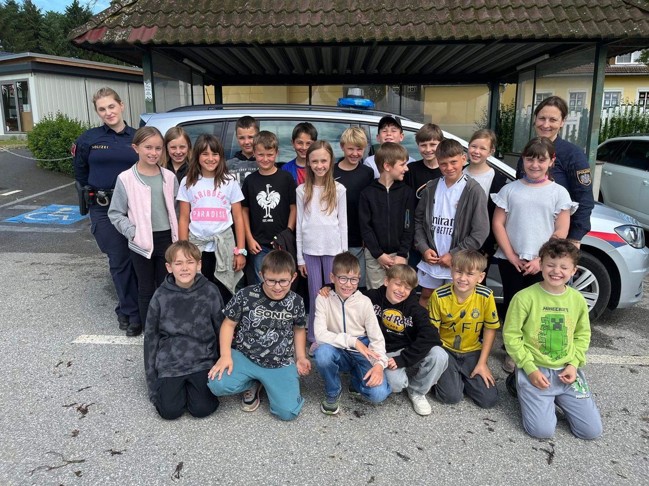 Eine Gruppe von Kindern und zwei Polizeibeamtinnen posiert für ein Foto vor einem Polizeiauto.