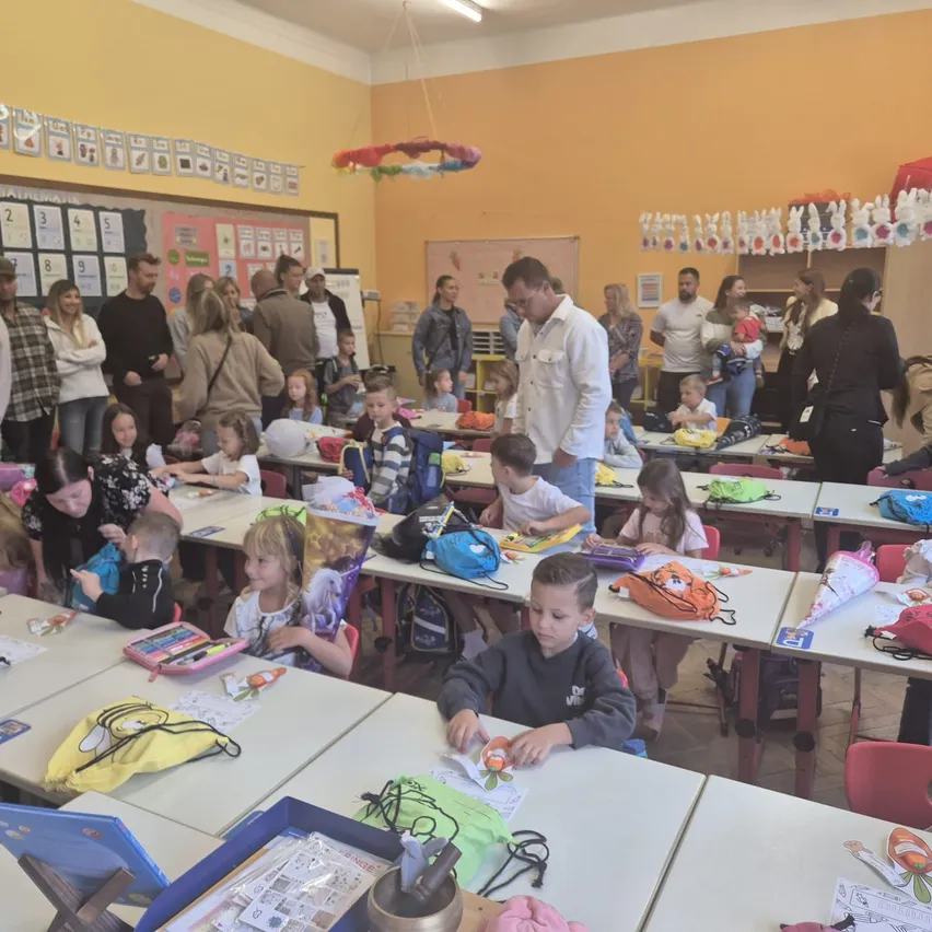 Ein Klassenzimmer voller Kinder und Erwachsener, einige stehen, einige sitzen und beschäftigen sich mit verschiedenen Aktivitäten.