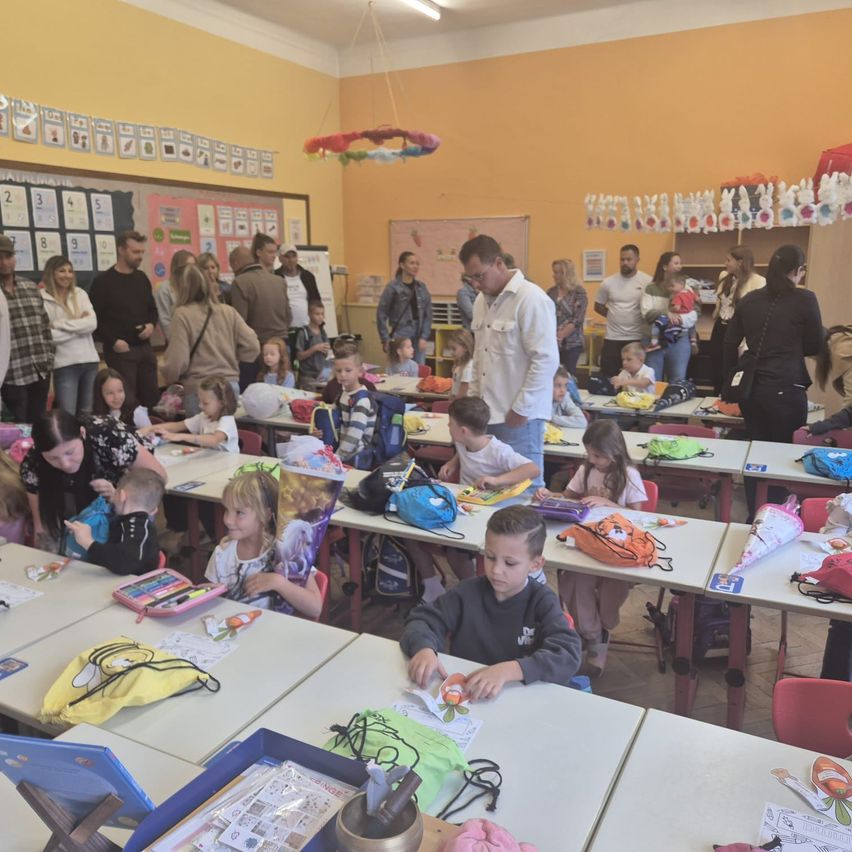 Ein Klassenzimmer voller Kinder und Erwachsener, einige stehen, einige sitzen und beschäftigen sich mit verschiedenen Aktivitäten.