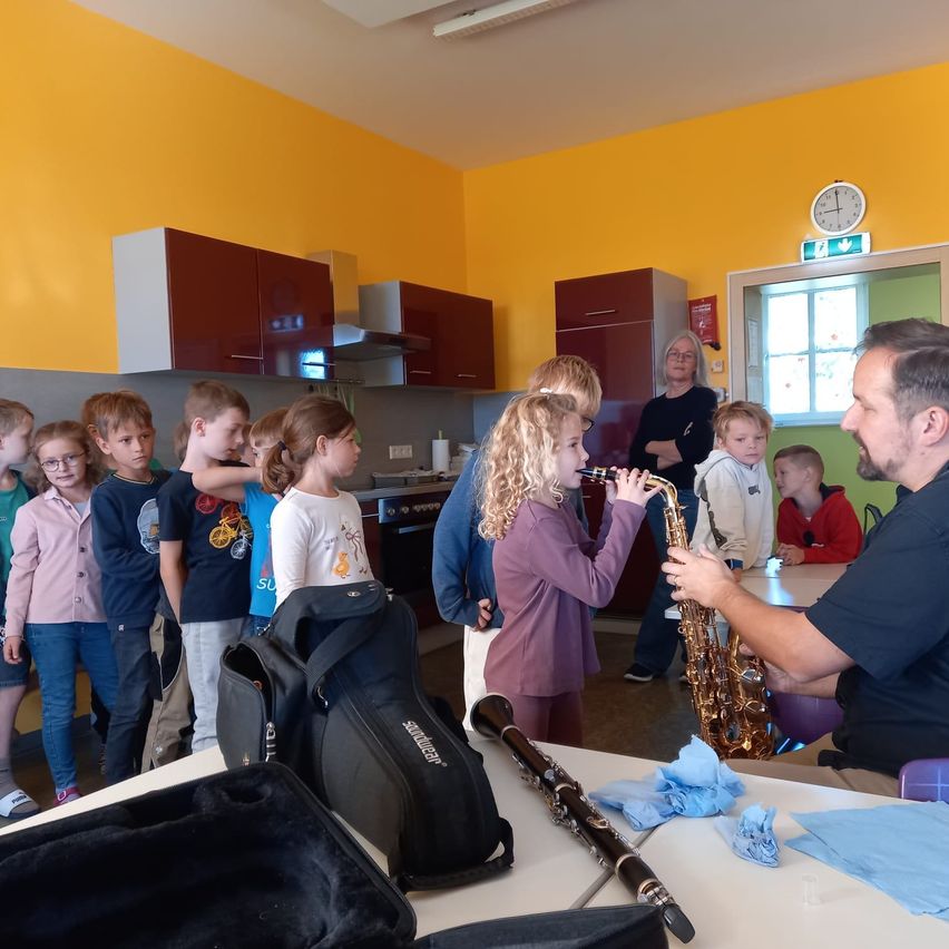 Ein Mann spielt Saxophon, während eine Gruppe von Kindern zuschaut.