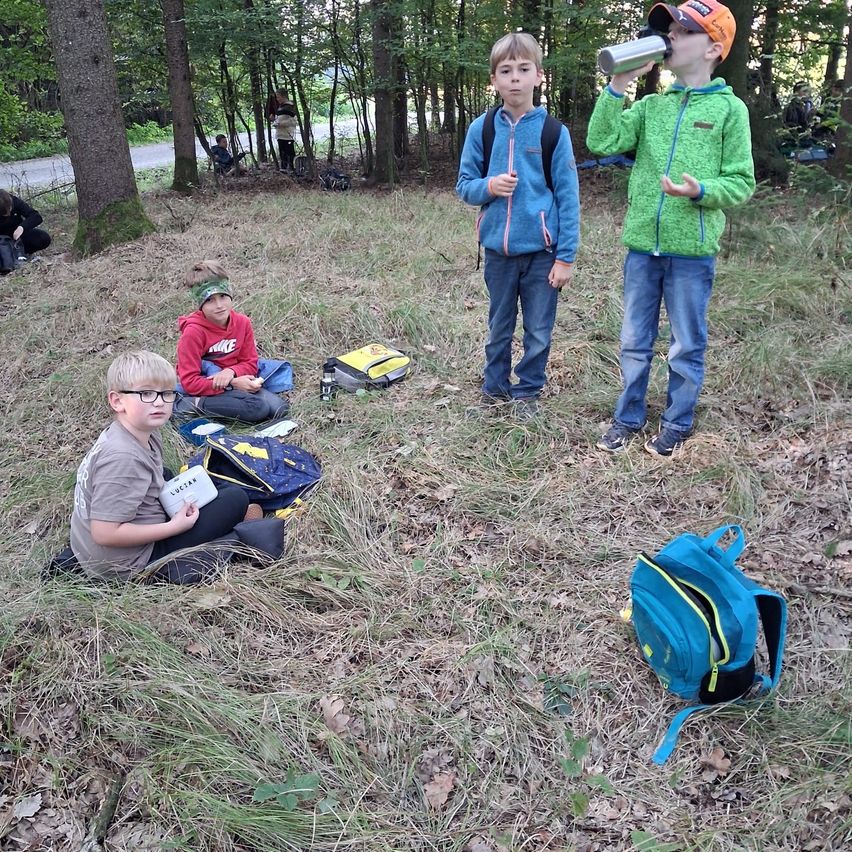 Vier Jungen sitzen auf dem Boden in einem Wald. Ein Junge trinkt aus einem Edelstahlbecher.