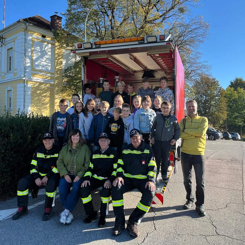 Eine Gruppe von Feuerwehrleuten und Kindern posiert für ein Foto vor einem Feuerwehrwagen.
