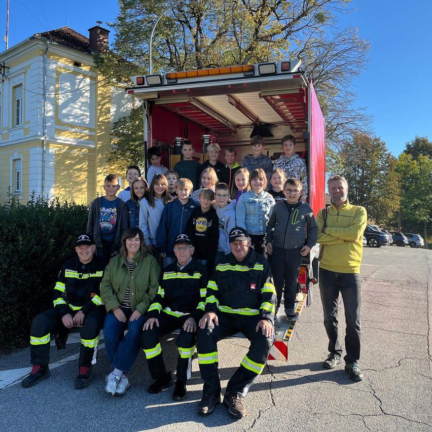 Eine Gruppe von Feuerwehrleuten und Kindern posiert für ein Foto vor einem Feuerwehrwagen.